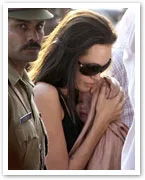 I don't know who the person is, but a woman wearing sunglasses holds a baby closely, with a man in uniform nearby.