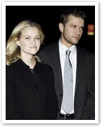 A man and a woman walking together, both dressed in formal black and white attire, in an outdoor evening setting.