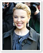 A person smiling at an event, wearing earrings and a dark outfit, surrounded by photographers.
