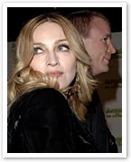 Madonna and a man attending an event, both looking to the side, with dim lighting in the background.