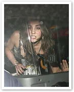 A woman with long hair, in a car at night, looks outward through the window.