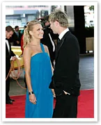 A couple in formal attire shares a moment on the red carpet at an event.