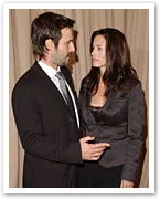 A man and a woman in formal attire are engaged in a serious conversation indoors.