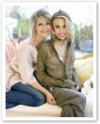 Two women seated together, smiling warmly, wearing stylish casual clothing with a light, airy background.