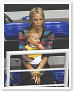 Young woman seated with a baby on her lap at a sports event, blue stadium seats in the background.