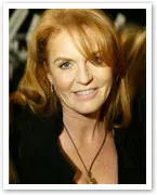 Woman with red hair smiling, wearing a black top and necklace, close-up portrait.