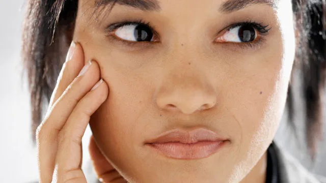 A woman gently touches her cheek, focusing intently, possibly examining her skin for acne scars.