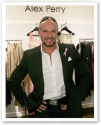 Designer Alex Perry stands smiling in front of a display of elegant dresses.