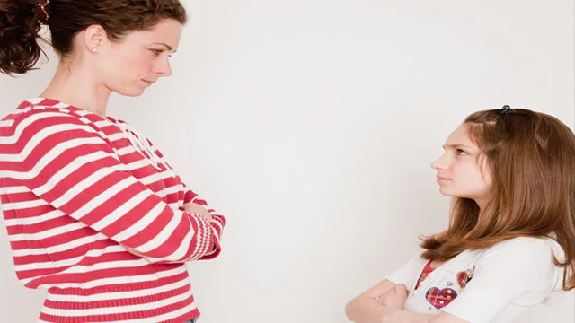A woman and a young girl face each other with arms crossed, both displaying serious expressions.