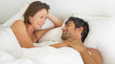 A couple smiling and talking while lying in bed, emphasizing connection in a relationship.