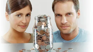 Man and woman looking at a jar full of coins on a table, emphasizing saving habits.