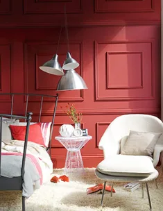 Cozy bedroom with a striking red feature wall, metal bed, pendant lights, armchair, and side table with decor items.
