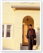 Man in leather jacket leaving a house, holding a briefcase.