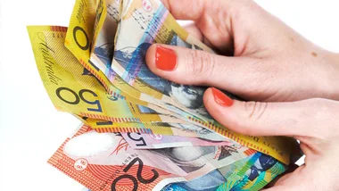 A person with red nail polish counting a stack of Australian banknotes.