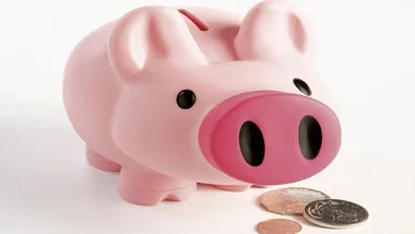 Pink piggy bank with a few coins spread in front on a white surface.