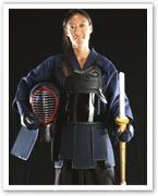 A person in Kendo gear holds a shinai sword and helmet, wearing traditional protective armor against a black background.