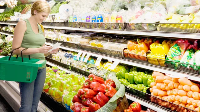Woman with shopping basket checking list in grocery store produce aisle.