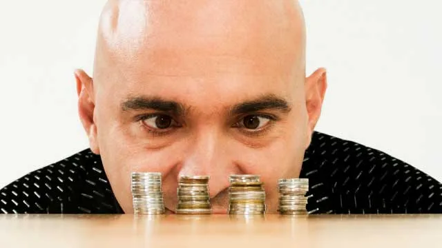 Bald man intensely observing stacks of coins on a table.