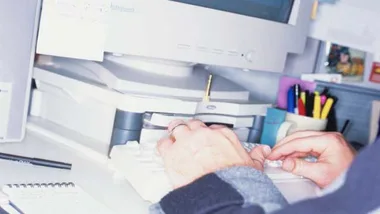 User typing on a keyboard in front of an old computer monitor, with office supplies in the background.