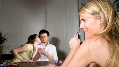Poker game with three players; two whispering; one woman smiling and holding cards.