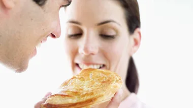 A man offers a smiling woman a pastry, engaging in a light-hearted moment.