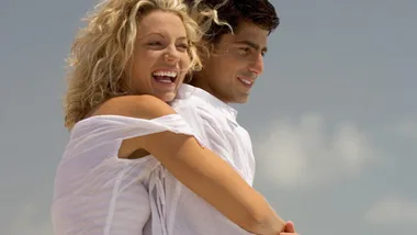 A couple embracing and smiling outdoors on a sunny day with a clear blue sky in the background.