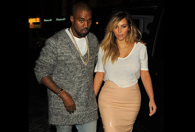 Couple walking in Paris at night; woman in white top and beige skirt, man in gray sweater, gold chain, and blue jeans.