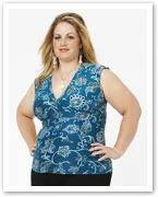 A woman with long, blonde hair wearing a blue patterned sleeveless top stands confidently against a light background.
