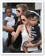 A couple carrying two children, one in each of their arms, outdoors with sunglasses.