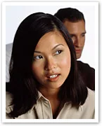 Young woman with dark hair looking to the side, man in the background, both wearing casual clothing.