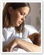 A woman in a hospital gown holding a newborn baby, looking down tenderly.