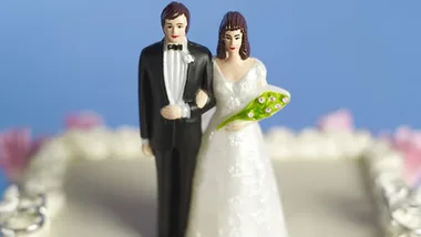 Bride and groom figurines on a wedding cake with a blue background.