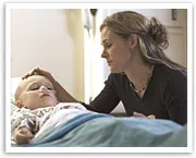 A woman gently touches a sleeping child's head in a hospital bed.