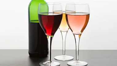 Wine bottle with three glasses of red, white, and rosé wine on a table.