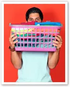 Man holding a pink laundry basket full of colorful folded clothes against an orange background.