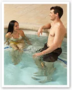 Man and woman chatting in a swimming pool, both wearing swimwear.