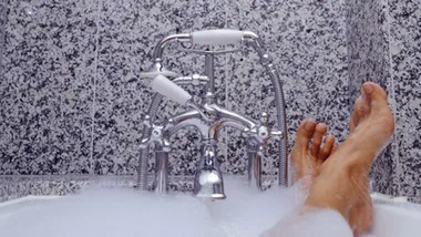 Bathtub faucet with foam, feet visible, against granite wall.