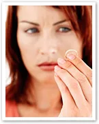A woman holding a ring, looking at it thoughtfully.