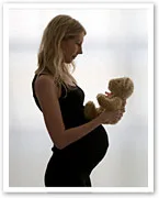 Pregnant woman in profile holding a teddy bear, wearing a black dress.
