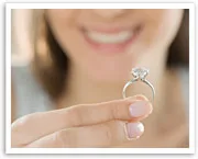 A person smiling while holding up a diamond ring, focusing on the jewelry.