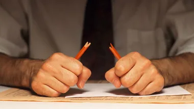 A person sitting at a desk, snapping a pencil in half out of frustration.