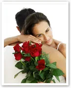 Woman embracing a man while holding a bouquet of red roses.