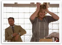 A woman in an apron looks distressed in a kitchen, while a man in a suit checks his watch in the background.