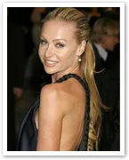 A person with long blonde hair in a black dress, smiling over their shoulder at an event.