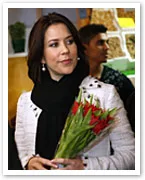 A woman in a white jacket holds a bouquet of red tulips, with a softly focused background.