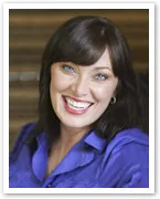A woman with dark hair and a bright smile wearing a purple top.