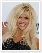 Blonde woman with voluminous hair wearing a black dress, smiling at a red carpet event.