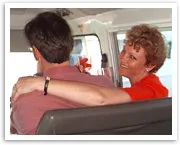 A woman in red smiles, embracing a man in a vehicle.