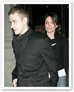 Alt text: "A man in a black jacket walking with a woman in a black top, both in an urban setting."