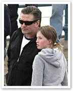 Man in sunglasses with a young girl in a hoodie standing close outdoors.